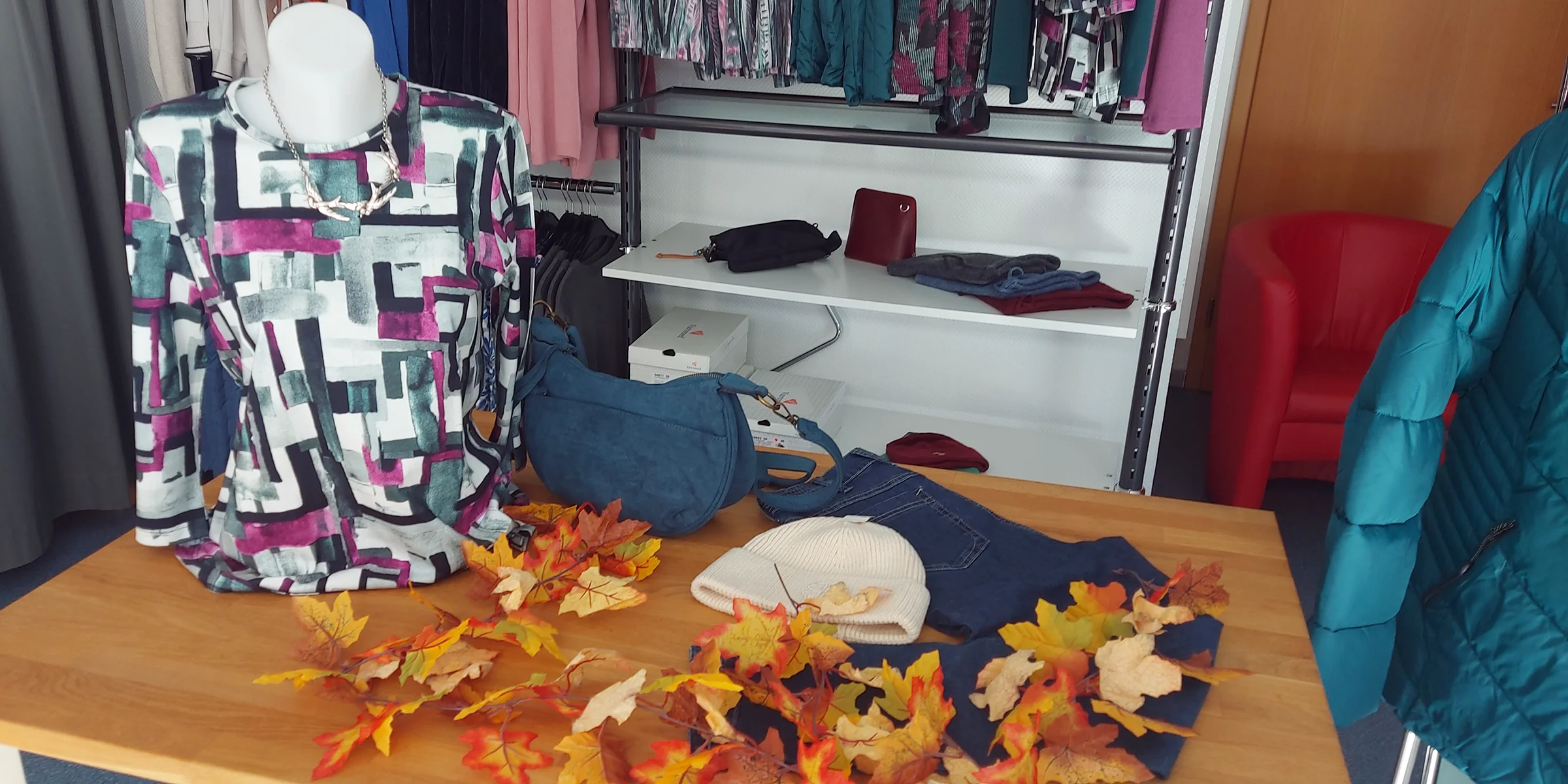 Herbstlich dekorierter Tisch mit Oberteilen, Hosen und Accessoires bei MODE Jörger
